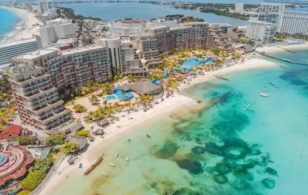 High-angle aerial view of a luxury beachfront resort in Cancun, featuring turquoise Caribbean waters, white sand beaches, and the Nichupté Lagoon in the background.