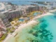 High-angle aerial view of a luxury beachfront resort in Cancun, featuring turquoise Caribbean waters, white sand beaches, and the Nichupté Lagoon in the background.