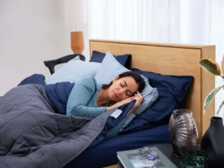 A woman sleeping soundly on a supportive mattress with navy blue and grey bedding, illustrating the goal of choosing the right sleep surface.