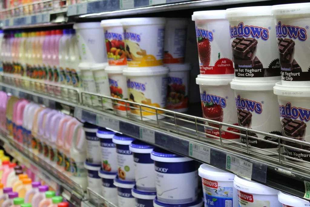 A grocery store refrigerated shelf stocked with various brands of yogurt and bottled dairy drinks.