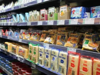A fully stocked refrigerator shelf in a grocery store featuring various brands of packaged cheese including Parmalat, White Rock, and Food Lover's. The image illustrates high inventory levels where demand forecasting is essential to prevent food waste.