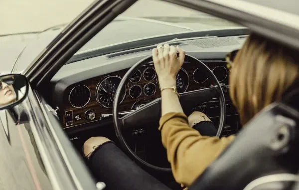 Interior view of a driver's perspective in a classic car, showing proper hand placement on the steering wheel and seated posture to prevent back pain during daily travel.