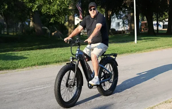 A man riding a grey fat tire e-bike with 4-inch wide knobby tires on a paved suburban road.