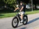 A man riding a grey fat tire e-bike with 4-inch wide knobby tires on a paved suburban road.