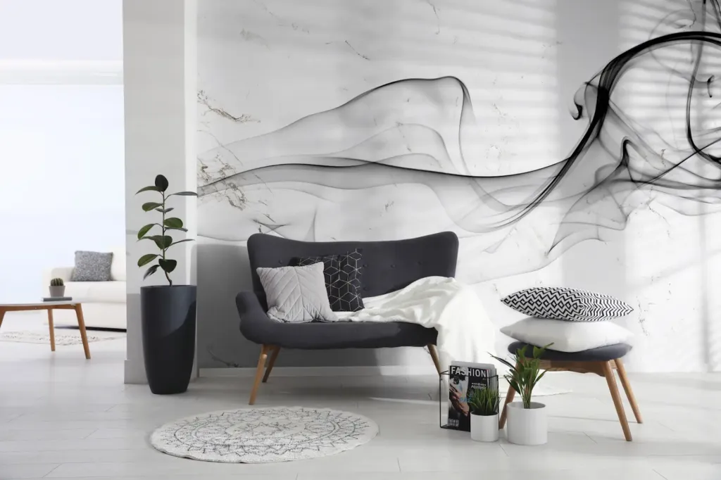 A stylish living room featuring a large-scale wall mural with flowing black smoke patterns over a white marble background. A dark gray mid-century modern sofa sits in front of the wall, accented by a white throw and geometric pillows.