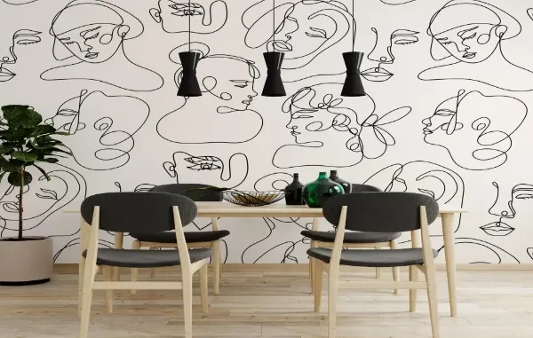 A modern dining room featuring a bold black and white wallpaper with continuous line art of abstract faces, paired with light wood furniture and black pendant lights.