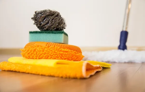 A stack of colorful cleaning supplies including a steel wool pad, sponges, and microfiber cloths on a hardwood floor for move-out cleaning in Chicago.