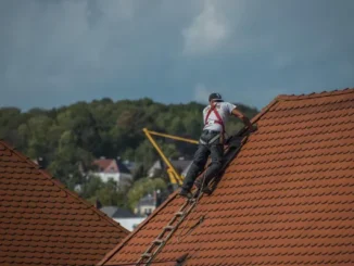 A professional contractor from a roofing company in Austin wearing a safety harness while inspecting a terracotta tile roof on a clear day.