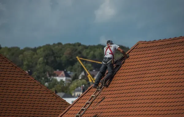 A professional contractor from a roofing company in Austin wearing a safety harness while inspecting a terracotta tile roof on a clear day.