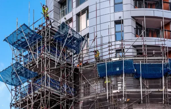 Professional siding contractors in safety gear working on a complex scaffolding system against a modern gray high-rise building.