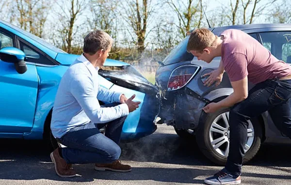Two men inspecting the front and rear bumper damage of a blue car and a grey car after a road accident.