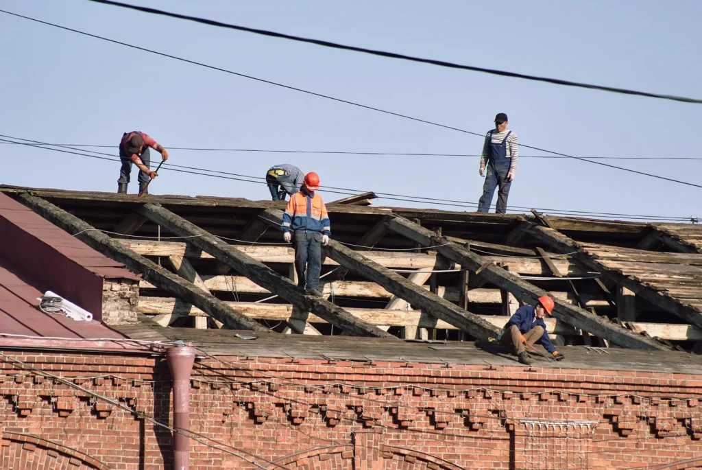 A team of professional roofing contractors repairing a damaged roof structure on a brick building to prevent further structural degradation and water damage.