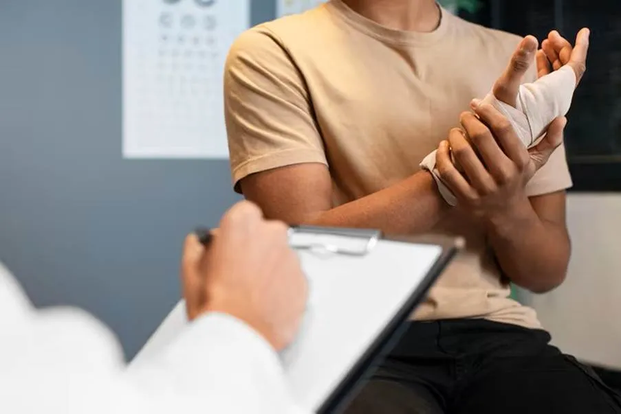 A patient with a bandaged wrist and hand consulting with a legal or medical professional who is taking notes on a clipboard, representing the initial stages of a personal injury claim.