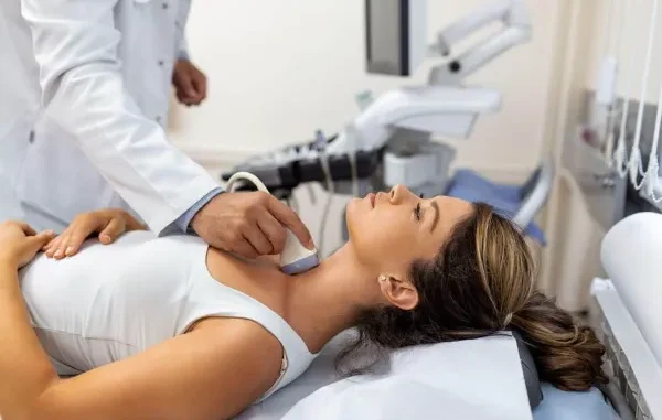 A medical professional performing an ultrasound on a woman's neck to examine the thyroid gland.