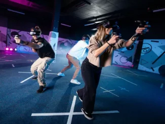 Three people wearing VR headsets and holding controllers while engaging in a multiplayer virtual reality experience at a modern indoor theme park facility.