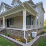 Exterior of a Charlotte home featuring a wrap-around porch, brick foundation, and a clean white gutter system with downspout extensions to prevent water damage.