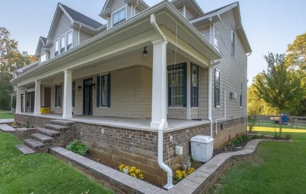 Exterior of a Charlotte home featuring a wrap-around porch, brick foundation, and a clean white gutter system with downspout extensions to prevent water damage.