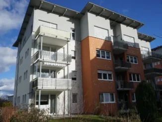 A multi-story apartment building with significant water and impact damage to its white and orange facade, showing peeling paint and pitted stucco.