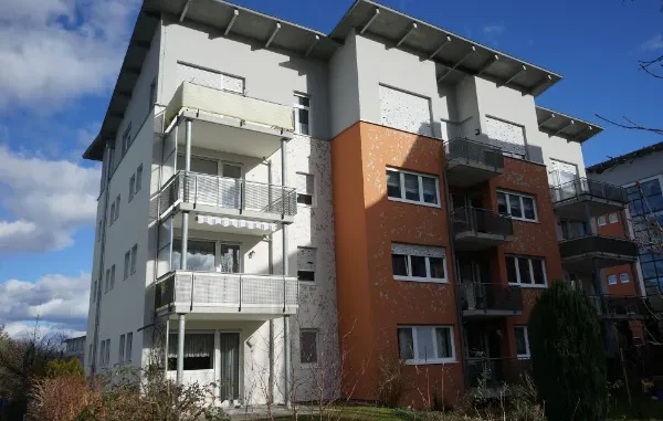 A multi-story apartment building with significant water and impact damage to its white and orange facade, showing peeling paint and pitted stucco.