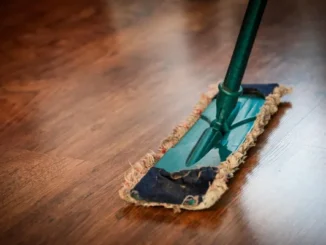 A close-up of a professional microfiber mop being used to clean a polished dark wood floor in an office setting.