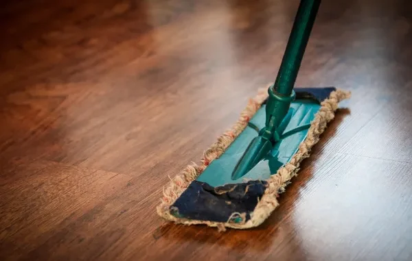 A close-up of a professional microfiber mop being used to clean a polished dark wood floor in an office setting.