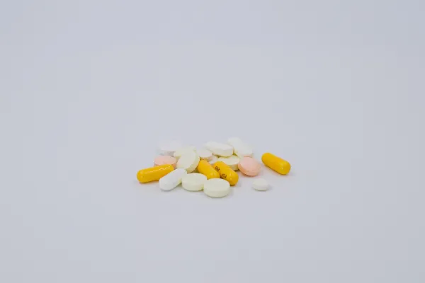 A small pile of various nutritional supplements, including yellow capsules and round white and peach-colored tablets, on a clean white background.