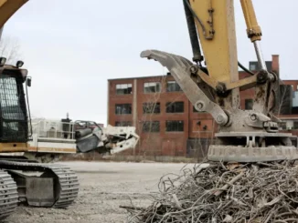 A heavy-duty excavator using a large industrial circular electromagnet to lift and sort a pile of twisted metal scrap at a construction site.