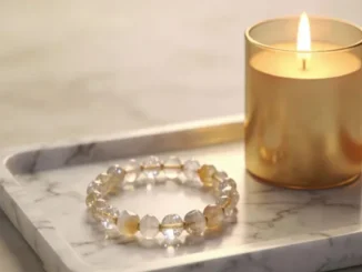 A handmade custom bracelet featuring clear and amber-toned faceted gemstone beads, resting on a white marble tray next to a glowing gold candle.