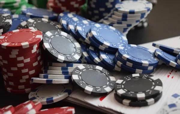High-angle shot of stacked red, blue, and black casino chips on a table next to a deck of playing cards, representing strategic betting.