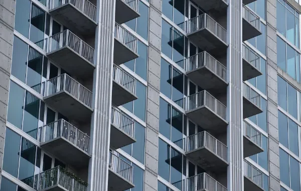 A close-up, low-angle shot of a modern high-rise apartment building featuring glass facades, concrete pillars, and multiple balconies.