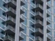 A close-up, low-angle shot of a modern high-rise apartment building featuring glass facades, concrete pillars, and multiple balconies.