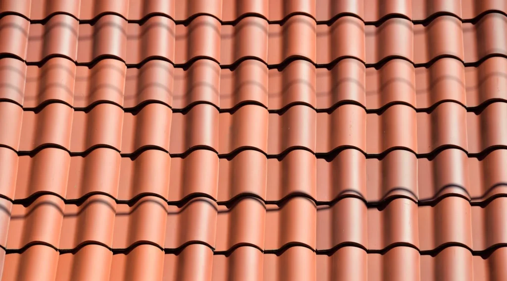 A close-up, high-angle view of rows of interlocking red terracotta clay roof tiles showing a uniform wave pattern and shadows.