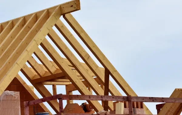 Close-up of a wooden roof truss system and rafters on a new residential construction site against a clear sky.