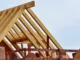 Close-up of a wooden roof truss system and rafters on a new residential construction site against a clear sky.