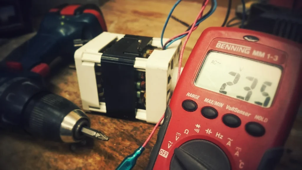 A close-up of a red Benning MM 1-3 digital multimeter displaying a reading of 235V AC on a wooden workbench next to an electric motor component and a cordless drill.