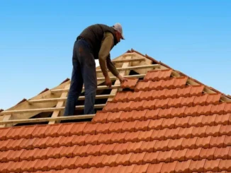 A professional roofer carefully installing terracotta clay tiles on a wooden roof frame against a clear blue sky.