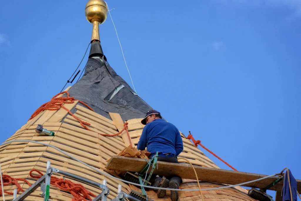 Skilled Roofer Installing Wood Shingles on a Steep Steeple