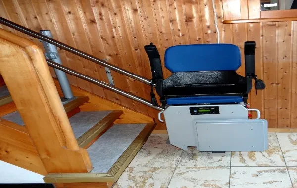 A modern blue and grey motorized stair lift installed on a dual-rail system alongside a wooden staircase in a home.