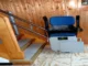 A modern blue and grey motorized stair lift installed on a dual-rail system alongside a wooden staircase in a home.
