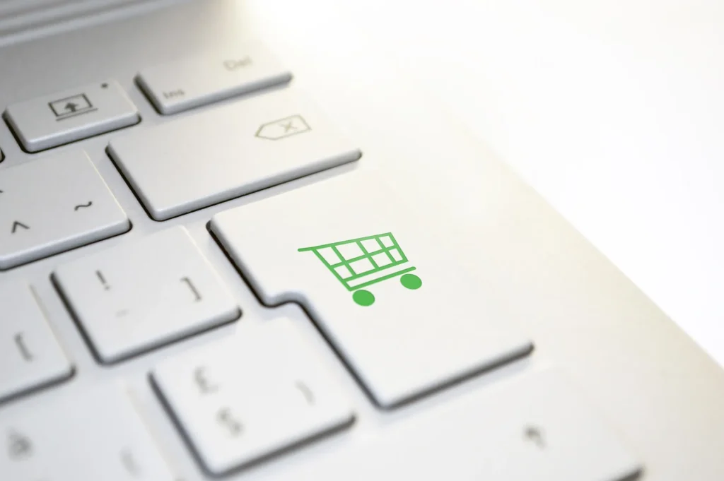 A close-up of a white laptop keyboard featuring a green shopping cart icon on the Enter key, symbolizing a completed online purchase.