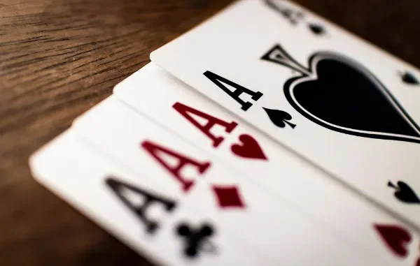 A close-up, shallow depth-of-field shot of four Aces fanned out on a wooden table, featuring the Ace of Spades, Hearts, Diamonds, and Clubs.