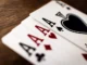 A close-up, shallow depth-of-field shot of four Aces fanned out on a wooden table, featuring the Ace of Spades, Hearts, Diamonds, and Clubs.