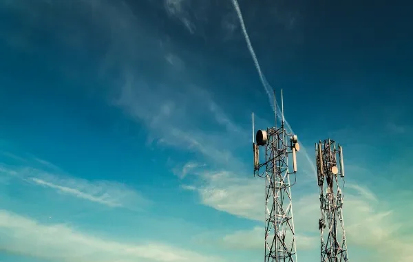 Two tall metal lattice telecommunication towers equipped with various antennas and satellite dishes against a blue sky with thin clouds.