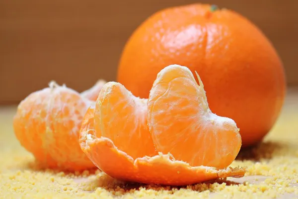 A close-up of a peeled tangerine showing juicy orange segments next to a whole unpeeled tangerine on a textured surface.