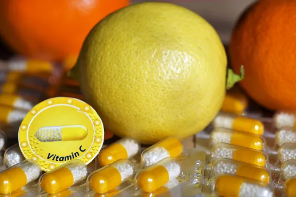 A whole fresh yellow lemon placed on top of several blister packs of yellow and white Vitamin C capsules.