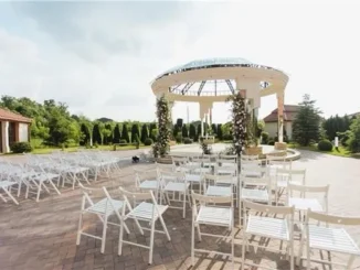 An upscale outdoor event venue featuring rows of white folding chairs facing a grand, circular pavilion rotunda adorned with floral arrangements, ideal for a modern corporate retreat or team event.