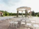 An upscale outdoor event venue featuring rows of white folding chairs facing a grand, circular pavilion rotunda adorned with floral arrangements, ideal for a modern corporate retreat or team event.