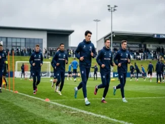 Professional soccer players jogging during a training session on a grass field, wearing matching navy blue Nike football tracksuits, training jackets, and pants.