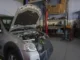 A silver BMW 3 Series with its hood open undergoing engine diagnostics and performance repair inside a professional automotive workshop.