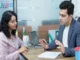 A professional insurance advisor in a blazer gestures while explaining policy details to a woman seated across a desk in a modern office.